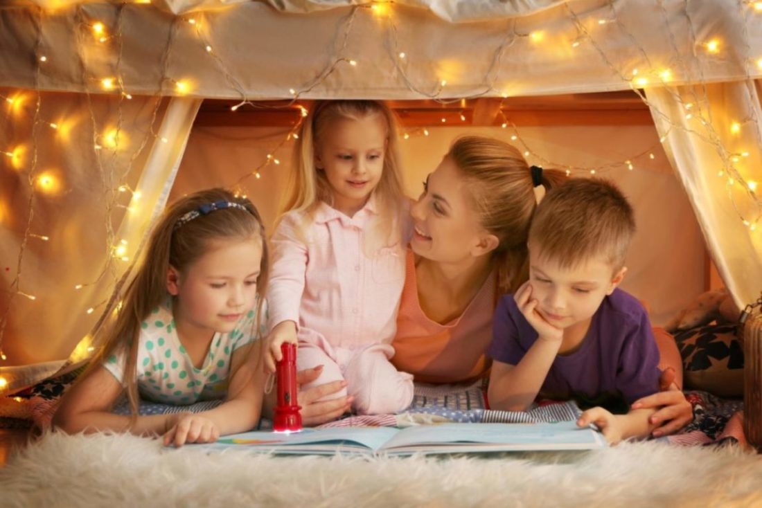 A happy family reading a book inside of a blanket fort.